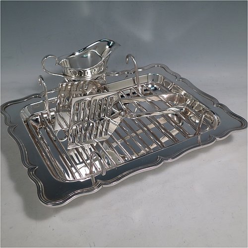 An Antique Edwardian Silver Plated asparagus serving set, having a plain rectangular body, with an applied and shaped reeded border, a wire-work serving rack, a sauce boat sat in a frame with loop handle, a pair of asparagus server tongs, and all sitting on a base with four button feet. All pieces were made by the Atkins Brothers of Sheffield in ca. 1900. The dimensions of this fine hand-made silver-plated asparagus serving set are length 29 cms (11.5 inches), and width, 23 cms (9 inches).    