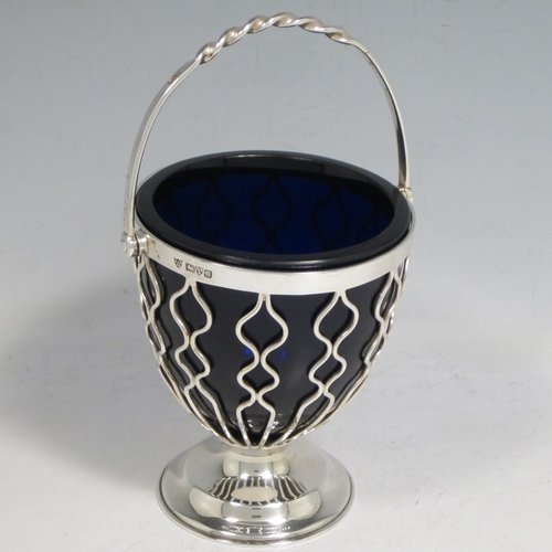 Antique Edwardian sterling silver sweet-meat basket, having a round tapering wire-work body, a  hinged and twisted swing handle, sitting on a plain round pedestal foot, and with an original blue-glass liner. Made by Hukin & Heath of Birmingham in 1902. The dimensions of this fine hand-made silver sweet-meat basket are height inc. handle 15 cms (6 inches), diameter at lip 8.5 cms (3.3 inches), and it weighs approx. 128g (4 troy ounces).   