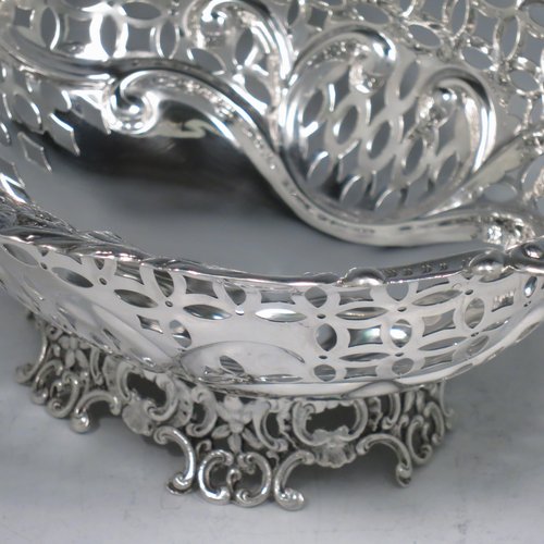 An Antique Edwardian pair of Sterling silver table baskets, having oval bodies with hand-pierced scroll-work decoration, with hand-chased floral borders, and sitting on matching pierced & scroll feet. Made by Charles Boyton of London in 1902. The dimensions of this fine pair of antique silver baskets are length 27 cms (10.75 inches), width 18.5 cms (7.25 inches), height 9 cms (3.5 inches), and they weigh a total of approx. 586g (19 troy ounces).   