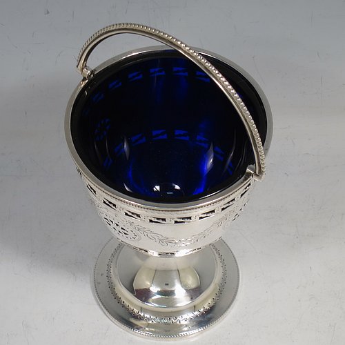 An Antique Edwardian Sterling Silver sweet-meat basket, having a round body with tapering sides all hand-engraved and hand-pierced with neoclassical style decoration, a hinged swing handle with applied bead-work, sitting on a round pedestal foot, and with an original blue-glass liner. Made by Thomas Bradbury of London in 1902. The dimensions of this fine hand-made antique silver sweet-meat basket are height inc. handle 16 cms (6.25 inches), diameter at lip 8.5 cms (3.3 inches), and it weighs approx. 140g (4.5 troy ounces).    