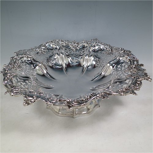 An Antique early Victorian large Sterling Silver table basket, having a round body with hand-pierced floral decoration within melon fluted panels, an applied cast floral and scroll border, and sitting on a melon fluted pedestal foot. Made by the Barnard Brothers of London in 1845. The dimensions of this fine hand-made antique silver basket are diameter 36 cms (14.25 inches), height 11 cms (4.25 inches), and it weighs approx. 1,082g (35 troy ounces).    