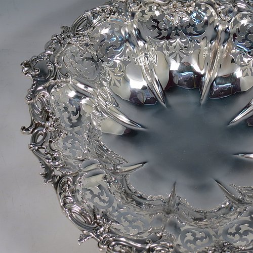 An Antique early Victorian large Sterling Silver table basket, having a round body with hand-pierced floral decoration within melon fluted panels, an applied cast floral and scroll border, and sitting on a melon fluted pedestal foot. Made by the Barnard Brothers of London in 1845. The dimensions of this fine hand-made antique silver basket are diameter 36 cms (14.25 inches), height 11 cms (4.25 inches), and it weighs approx. 1,082g (35 troy ounces).    