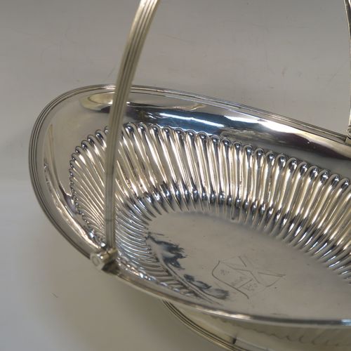 A very handsome Antique Georgian Sterling Silver basket, having an oval body with an applied reeded border, with hand-chased fluted decoration, a hinged and reeded swing handle, all sitting on a plain oval collet foot. This elegant antique silver basket was made by Joseph Scammell of London in 1795. The dimensions of this fine hand-made antique silver basket are height 28 cms (11 inches), length 37 cms (14.5 inches), width 26 cms (10.25 inches), and it weighs approx. 899g (29 troy ounces). Please note that this basket is crested.   