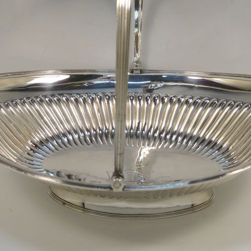 A very handsome Antique Georgian Sterling Silver basket, having an oval body with an applied reeded border, with hand-chased fluted decoration, a hinged and reeded swing handle, all sitting on a plain oval collet foot. This elegant antique silver basket was made by Joseph Scammell of London in 1795. The dimensions of this fine hand-made antique silver basket are height 28 cms (11 inches), length 37 cms (14.5 inches), width 26 cms (10.25 inches), and it weighs approx. 899g (29 troy ounces). Please note that this basket is crested.   