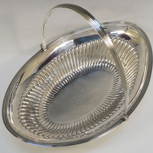 A very handsome Antique Georgian Sterling Silver basket, having an oval body with an applied reeded border, with hand-chased fluted decoration, a hinged and reeded swing handle, all sitting on a plain oval collet foot. This elegant antique silver basket was made by Joseph Scammell of London in 1795. The dimensions of this fine hand-made antique silver basket are height 28 cms (11 inches), length 37 cms (14.5 inches), width 26 cms (10.25 inches), and it weighs approx. 899g (29 troy ounces). Please note that this basket is crested.   