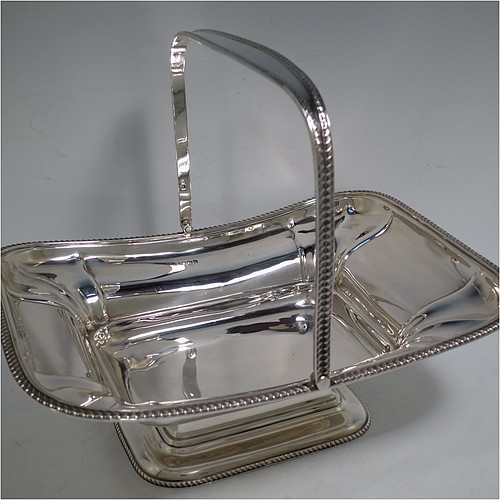 An Antique Edwardian Sterling Silver basket, having a rectangular body, with an applied gadroon border, a hinged and swing handle with gadroon edges, all sitting on a pedestal foot. Made by the Dixon Brothers of Sheffield in 1910. The dimensions of this fine hand-made antique silver basket are height 23 cms (9 inches), length 27.5 cms (10.75 inches), width 21 cms (8.25 inches), and it weighs approx. 746g (24 troy ounces).    