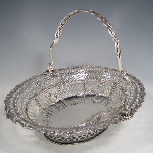 Antique Georgian sterling silver hand-pierced basket with swing-handle, having bands of floral piercing divided by hand-chased bead-work, an applied cast floral border, a cast floral swing-handle, and sitting on a pierced collet foot with rope-twist border. Made by Richard Mills of London in 1772. The dimensions of this fine hand-made silver basket are length 30.5 cms (12 inches), width 27.5 cms (10.75 inches), height 28 cms (11 inches), and it weighs approx. 937g (30 troy ounces).