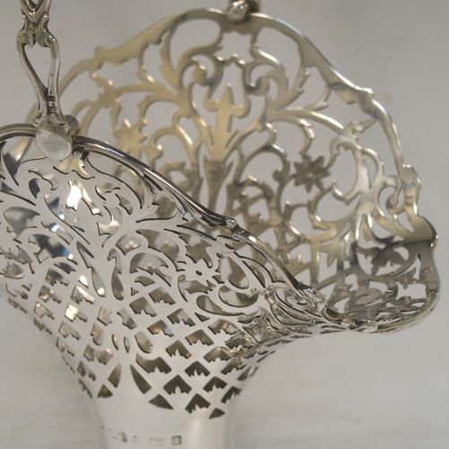 A very pretty Antique Edwardian Sterling Silver wedding style basket, having an oval body with applied scroll borders and hand-pierced floral and geometrical decoration, and a matching swing handle, all sitting on a pedestal foot. This beautiful silver wedding basket was made in Birmingham in 1910. The dimensions of this fine hand-made antique silver wedding basket are height 23 cms (9 inches), length 15 cms (6 inches), width 11.5 cms (4.5 inches), and it weighs approx. 243g (7.8 troy ounces).   