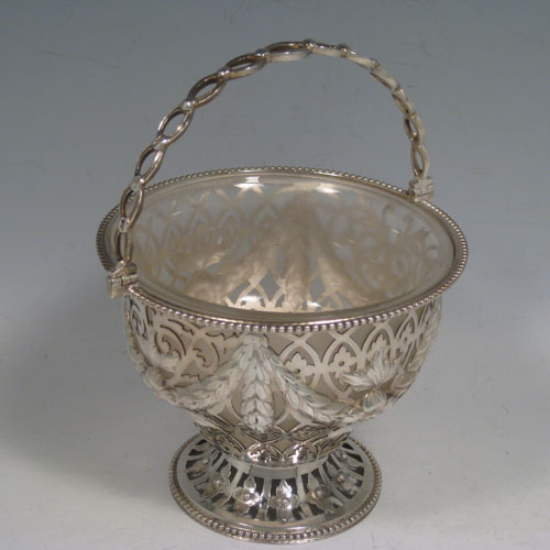 Antique Victorian sterling silver sweetmeat basket, having a round hand-pierced and chased body with floral decoration bead-edged borders, loop and knot handle, frosted glass liner, and sitting on a pierced pedestal foot. Made by the William Savory of London in 1863. Height including handle 18 cms (7 inches), diameter 13 cms (5 inches). Weight approx. 267g (8.6 troy ounces).