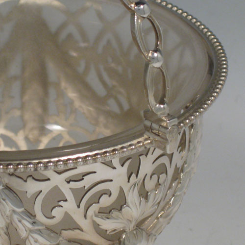 Antique Victorian sterling silver sweetmeat basket, having a round hand-pierced and chased body with floral decoration bead-edged borders, loop and knot handle, frosted glass liner, and sitting on a pierced pedestal foot. Made by the William Savory of London in 1863. Height including handle 18 cms (7 inches), diameter 13 cms (5 inches). Weight approx. 267g (8.6 troy ounces).