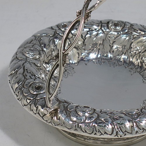 An Antique Victorian Sterling Silver sweet-meat basket, having a round body with hand-chased floral decoration, a hinged hand-pierced and chased swing handle, and all sitting on a plain round pedestal foot. Made by Henry Wilkinson & Co., of London in 1893. The dimensions of this fine hand-made antique silver basket are height 10 cms (4 inches), diameter 12.5 cms (5 inches), and it weighs approx. 147g (4.7 troy ounces).   