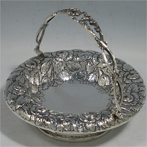 An Antique Victorian Sterling Silver sweet-meat basket, having a round body with hand-chased floral decoration, a hinged hand-pierced and chased swing handle, and all sitting on a plain round pedestal foot. Made by Henry Wilkinson & Co., of London in 1893. The dimensions of this fine hand-made antique silver basket are height 10 cms (4 inches), diameter 12.5 cms (5 inches), and it weighs approx. 147g (4.7 troy ounces).   