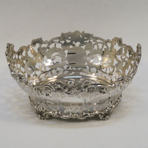 A very pretty Antique Scottish Edwardian Sterling silver small fruit basket, having an oval body with hand-pierced and engraved floral and scroll decoration, applied cast scroll and floral borders, and all sitting on four cast foliate feet. This beautiful antique silver basket was made by Hamilton and Inches of Edinburgh in 1904. The dimensions of this fine antique silver basket are length 20 cms (8 inches), width 17 cms (6.75 inches), height 10 cms (4 inches), and it weighs approx. 452g (14.6 troy ounces).   