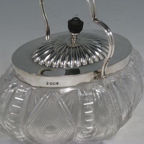 A very pretty Antique Victorian Sterling Silver and hand-cut crystal biscuit jar, having an unusual oval crystal body with hand-cut floral and geometric work, a lift-off lid with half-fluting and wooden finial, and a wire-work swing handle. Made by Fordham and Faulkner of Sheffield in 1901. The dimensions of this fine hand-made antique silver and crystal biscuit jar are height 18 cms (7 inches), length 20 cms (8 inches), and width 15 cms (6 inches).