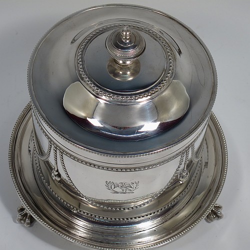 An Antique Victorian Silver Plated biscuit box, having a round body with applied bead-edged borders, straight sides and hand-chased swags of bead-work in a neoclassical style, a hinged domed lid with cast finial, and all sitting on an attached plate with three cast claw and ball feet. Made by James Thompson of Sheffield in ca. 1880. The dimensions of this fine hand-made antique silver-plated biscuit box are height 18 cms (7 inches), and diameter at base 18 cms (7 inches). Please note that this item is crested.