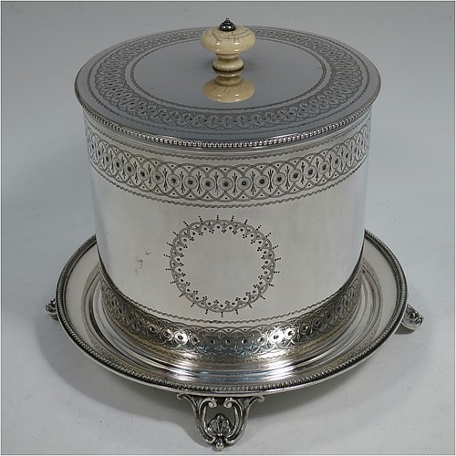 A very pretty Antique Victorian Silver Plated biscuit box, having a round body with straight sides and applied bead-edged borders, with very pretty hand-engraved bands of geometrical and floral work, a hinged flat lid with bone finial, and all sitting on an attached plate with four cast scroll and shell feet. Made by Elkington and Co., of Sheffield in ca. 1880. The dimensions of this fine hand-made antique silver-plated biscuit box are height 16 cms (6.3 inches), and diameter at base 18 cms (7 inches).    