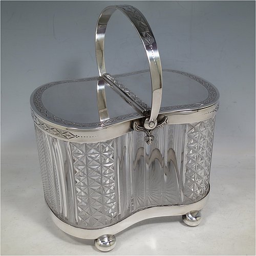 An Antique Victorian silver plated and cut crystal biscuit jar, having a hobnail and fluted cut  crystal body, a hand-engraved mechanically double-hinged lid with a swing handle, and all sitting on a base with four cushion feet. Made by Thomas Wilkinson & Sons of Sheffield in ca. 1890. The dimensions of this fine hand-made antique silver-plated and hand-cut crystal biscuit jar are height inc. handle 23 cms (9 inches), length of base 19 cms (7.5 inches), and width of base 14 cms (5.5 inches).   