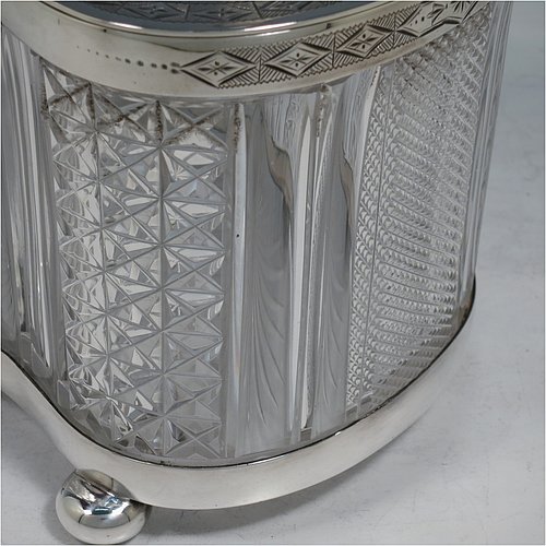 An Antique Victorian silver plated and cut crystal biscuit jar, having a hobnail and fluted cut  crystal body, a hand-engraved mechanically double-hinged lid with a swing handle, and all sitting on a base with four cushion feet. Made by Thomas Wilkinson & Sons of Sheffield in ca. 1890. The dimensions of this fine hand-made antique silver-plated and hand-cut crystal biscuit jar are height inc. handle 23 cms (9 inches), length of base 19 cms (7.5 inches), and width of base 14 cms (5.5 inches).   