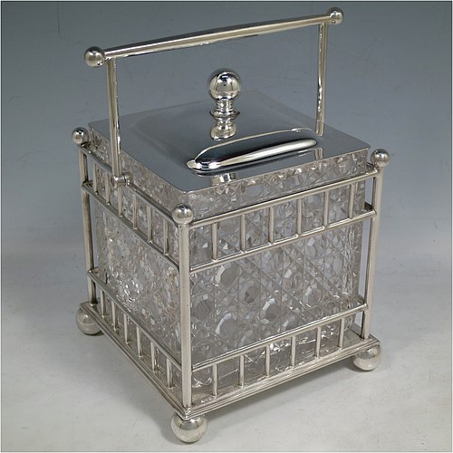 An Antique Victorian silver plated and cut crystal biscuit jar, having a hobnail cut square crystal jar with straight sides, a plain lift-off lid with ball finial, all inside a galleried wire-work frame with swing handle, and sitting on a base with four ball feet. Made by the Atkins Brothers of Sheffield in ca. 1880. The dimensions of this fine hand-made antique silver-plated and hand-cut crystal biscuit jar are height inc. handle 20 cms (8 inches), and 14 cms (5.5 inches) square.    