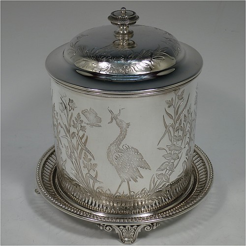 An Antique Victorian Silver Plated Chinoiserie style biscuit box, having a round body with straight sides and applied bead-edged borders, with very pretty hand-engraved flowers, reeds, birds, and butterfly work, a hinged domed lid with cast finial, and all sitting on a hand-pierced attached plate with four cast scroll feet. Made by the Atkin Brothers of Sheffield in ca. 1880. The dimensions of this fine hand-made antique silver-plated biscuit box are height 18 cms (7 inches), and diameter at base 17.5 cms (7 inches).    