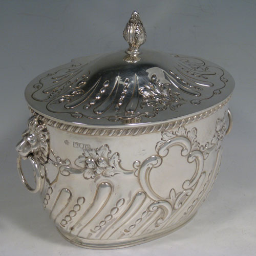    Antique Victorian sterling silver biscuit box, having an oval body with hand-chased fluting and floral decoration, hinged lid with finial, and two lion-mask ring handles. Height 18 cms (7 inches), length 18.5 cms (7.25 inches), width 13 cms (5 inches). Weight approx. 682g (22 troy ounces).