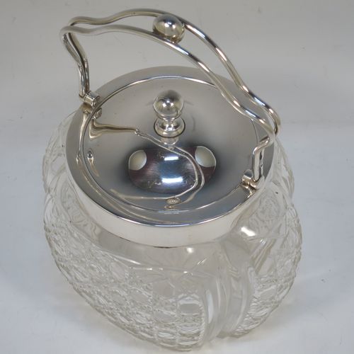 A pretty Antique Edwardian Sterling Silver and hand-cut crystal biscuit jar, having an unusual crystal body with hand-cut hobnail pattern panels with fluted corners, a plain round lift-off lid with a ball finial, a wire-work swing handle, and all sitting on a star-cut flat base. Made by Robert Pringle of London in 1904. The dimensions of this fine hand-made antique silver and crystal biscuit jar are height (excluding handle) 15 cms (6 inches), length 15 cms (6 inches), and width 13 cms (5 inches).  