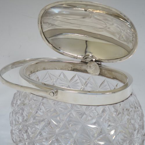 A very pretty and unusual Antique Victorian Sterling Silver and hand-cut crystal biscuit jar, having an oval crystal body with hand-cut hobnail and star-cut work, a plain oval mechanical lid which opens when moving the plain  hinged swing-handle either left or right, and all sitting on a flat star-cut base. Made by Heath and Middleton of Birmingham in 1899. The dimensions of this fine hand-made antique silver and crystal biscuit jar are height (excluding handle) 13 cms (5 inches), length 16.5 cms (6.5 inches), and width 9 cms (3.5 inches).  