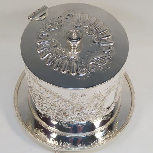 A very pretty Antique Victorian Silver-Plated biscuit box, having a round straight-sided body with bead-edged borders, hand-chased fluting, scroll, and floral decoration, a flat hinged lid with matching decoration and a cast round finial, and sitting on an attached base plate with three cast foliate feet. This beautiful antique silver-plated biscuit box was made by Harrison Brothers and Howson of Sheffield in ca. 1880. The dimensions of this fine hand-made antique silver-plated biscuit box are height 18 cms (7 inches), and diameter at base 19 cms (7.5 inches).  