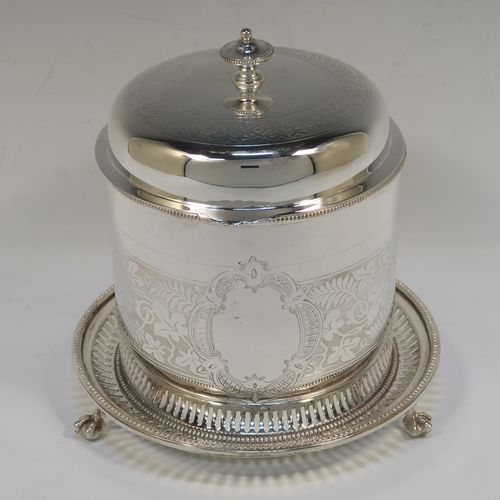 A very pretty Antique Victorian Silver-Plated biscuit box, having a round straight-sided body with bead-edged borders, hand-engraved floral decoration, a domed hinged lid with matching decoration and a cast round finial, and sitting on an attached base plate with three cast lions-paw  feet. This beautiful antique silver-plated biscuit box was made in ca. 1880. The dimensions of this fine hand-made antique silver-plated biscuit box are height 17 cms (6.75 inches), and diameter at base 18 cms (7 inches).   