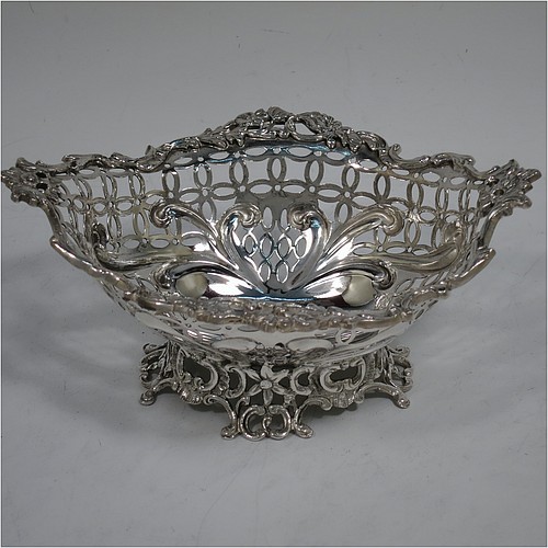 A very pretty Antique Victorian Sterling Silver pair of bon-bon baskets or dishes, having oval bodies with hand-pierced geometrical and scroll work decoration, an applied cast floral and scroll border, and sitting on matching pierced feet. Made by William Comyns of London in 1892. The dimensions of this fine hand-made pair of antique silver bon-bon dishes or baskets are length 16 cms (6.25 inches), width 12 cms (4.75 inches), height 7 cms (2.75 inches), and they weigh a total of  approx. 328g (10.6 troy ounces).    