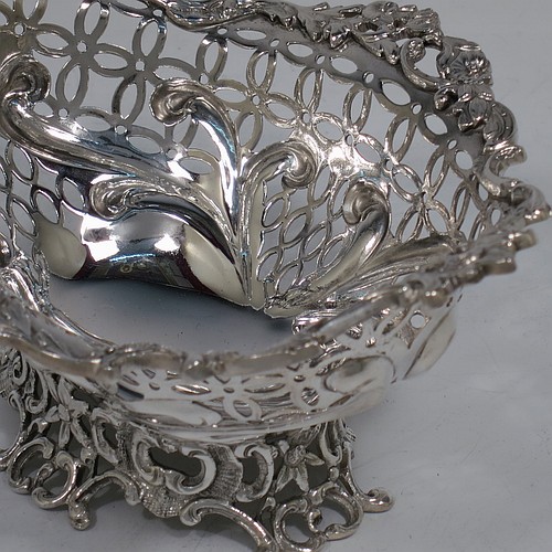 A very pretty Antique Victorian Sterling Silver pair of bon-bon baskets or dishes, having oval bodies with hand-pierced geometrical and scroll work decoration, an applied cast floral and scroll border, and sitting on matching pierced feet. Made by William Comyns of London in 1892. The dimensions of this fine hand-made pair of antique silver bon-bon dishes or baskets are length 16 cms (6.25 inches), width 12 cms (4.75 inches), height 7 cms (2.75 inches), and they weigh a total of  approx. 328g (10.6 troy ounces).    