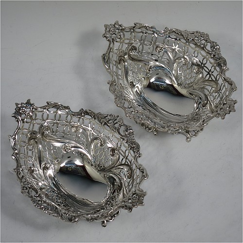 A very pretty Antique Victorian Sterling Silver pair of bon-bon baskets or dishes, having oval bodies with hand-pierced geometrical and scroll work decoration, an applied cast floral and scroll border, and sitting on matching pierced feet. Made by William Comyns of London in 1892. The dimensions of this fine hand-made pair of antique silver bon-bon dishes or baskets are length 16 cms (6.25 inches), width 12 cms (4.75 inches), height 7 cms (2.75 inches), and they weigh a total of  approx. 328g (10.6 troy ounces).    