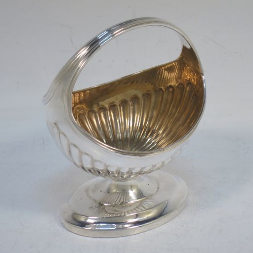 A small but very unusual and pretty Antique Georgian Sterling Silver bon-bon dish or sweet-meat basket, having an oval body with hand-chased half-fluted decoration, a gold-gilt interior, an overhead loop handle, and all sitting on a pedestal foot. Made in London in 1802. The dimensions of this fine hand-made antique bon-bon dish or basket are length 8 cms (3 inches), height 10 cms (4 inches), width 7 cms (2.75 inches), and it weighs approx. 104g (3.4 troy ounces)   