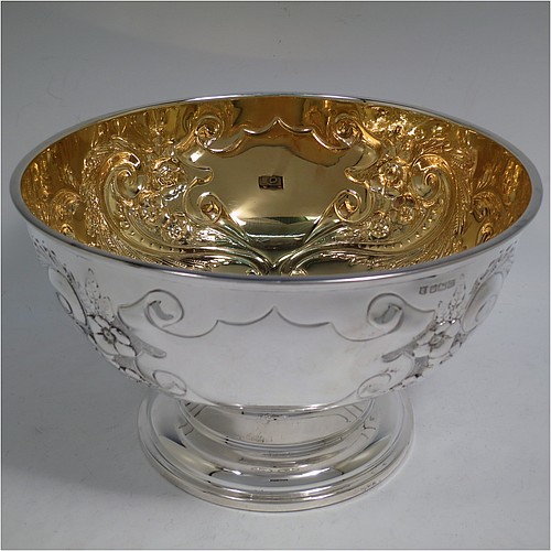 A very pretty Antique Edwardian Sterling Silver large table bowl, having a round body with an applied reeded border and hand-chased floral and scroll decoration, with two vacant cartouches either side, a gold-gilt interior, and all sitting on a stepped pedestal foot. Made by the Deakin Brothers of Sheffield in 1904. The dimensions of this fine hand-made antique silver bowl are diameter 25.5 cms (10 inches), height 15 cms (6 inches), and it weighs approx. 780g (25 troy ounces).    