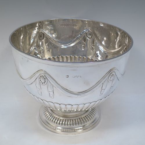 A very pretty Antique Victorian Sterling Silver large Rose bowl, having a round body with hand-chased half fluted decoration, an applied reeded rim above another band of hand-chased swags and bows, and sitting on a pedestal foot with matching fluting. Made by Gibson and Langman of London in 1890. The dimensions of this fine hand-made antique silver large table bowl are diameter 24 cms (9.5 inches), height 20 cms (8 inches), and it weighs approx. 965g (31 troy ounces).   