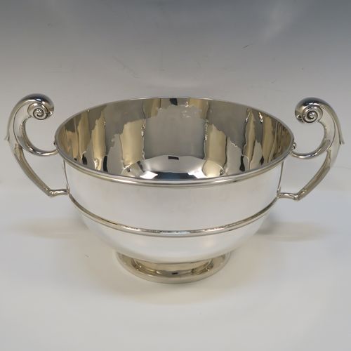 A large and very handsome Antique Edwardian Scottish Sterling Silver two-handled table bowl, having a plain round bellied body, with two cast flying scroll side-handles, an applied top border and central girdle, and all sitting on a plain round pedestal foot. This elegant traditional two-handled silver bowl or trophy was made by Lawson and Co., of Glasgow in 1902. The dimensions of this fine hand-made antique silver bowl are width across handles 37 cms (14.5 inches), diameter of main body 25.5 cms (10 inches), height 19 cms (7.5 inches), and it weighs approx. 1,532g (49.5 troy ounces).   