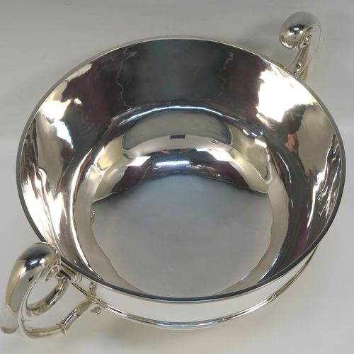 A large and very handsome Antique Edwardian Scottish Sterling Silver two-handled table bowl, having a plain round bellied body, with two cast flying scroll side-handles, an applied top border and central girdle, and all sitting on a plain round pedestal foot. This elegant traditional two-handled silver bowl or trophy was made by Lawson and Co., of Glasgow in 1902. The dimensions of this fine hand-made antique silver bowl are width across handles 37 cms (14.5 inches), diameter of main body 25.5 cms (10 inches), height 19 cms (7.5 inches), and it weighs approx. 1,532g (49.5 troy ounces).   