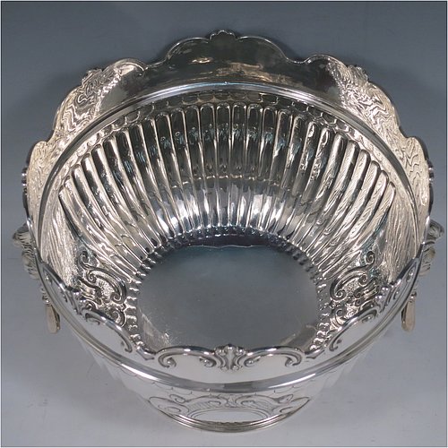 An Antique Edwardian Sterling Silver Montieth style bowl, having a round body with an applied scroll border, with hand-chased half-fluted decoration, together with two cast lion-mask side-handles, and sitting on a pedestal foot. Made by Elkington & Co.,of London in 1910. The dimensions of this fine hand-made antique silver table bowl are diameter 22 cms (8.75 inches), height 16.5 cms (6.5 inches), and it weighs approx. 930g (30 troy ounces).    