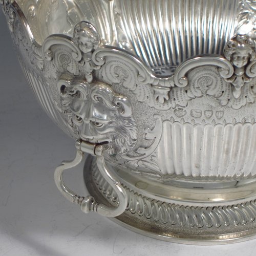 An Antique Victorian sterling silver Montieth style bowl, having a round body with an applied scroll and cast cherub-head border, with hand-chased floral and half-fluted decoration, together with two cast lion-mask and hinged side-handles, and sitting on a pedestal foot. Made by the Barnard Brothers of London in 1894. The dimensions of this fine hand-made silver table bowl are diameter 20 cms (8 inches), height 13 cms (5.25 inches), and it weighs approx. 653g (21 troy ounces).   