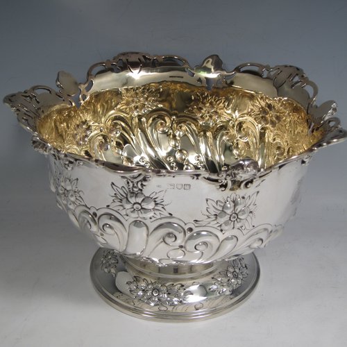 Antique Victorian sterling silver pair of rose bowls, having round hand-chased bodies with swirl fluting, scrolls, and floral decoration, with applied cast and pierced borders, gold gilt interiors, and sitting on pedestal feet. Made by Charles Edwards of London in 1901. The dimensions of these fine hand-made silver bowls are height 14 cms (5 inches), diameter 23 cms (9 inches), and they have a total weight of approx. 1,587g (51 troy ounces). Please note that both of these bowls are crested.