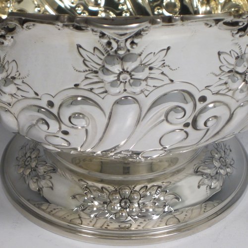 Antique Victorian sterling silver pair of rose bowls, having round hand-chased bodies with swirl fluting, scrolls, and floral decoration, with applied cast and pierced borders, gold gilt interiors, and sitting on pedestal feet. Made by Charles Edwards of London in 1901. The dimensions of these fine hand-made silver bowls are height 14 cms (5 inches), diameter 23 cms (9 inches), and they have a total weight of approx. 1,587g (51 troy ounces). Please note that both of these bowls are crested.