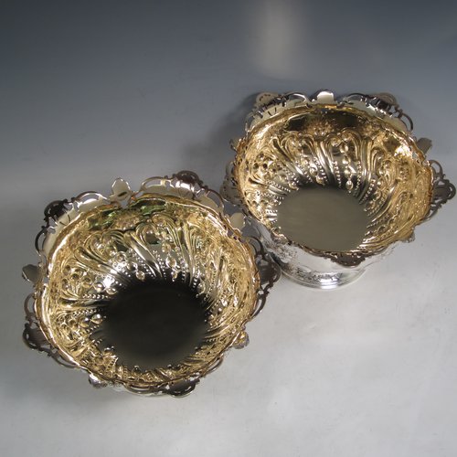 Antique Victorian sterling silver pair of rose bowls, having round hand-chased bodies with swirl fluting, scrolls, and floral decoration, with applied cast and pierced borders, gold gilt interiors, and sitting on pedestal feet. Made by Charles Edwards of London in 1901. The dimensions of these fine hand-made silver bowls are height 14 cms (5 inches), diameter 23 cms (9 inches), and they have a total weight of approx. 1,587g (51 troy ounces). Please note that both of these bowls are crested.