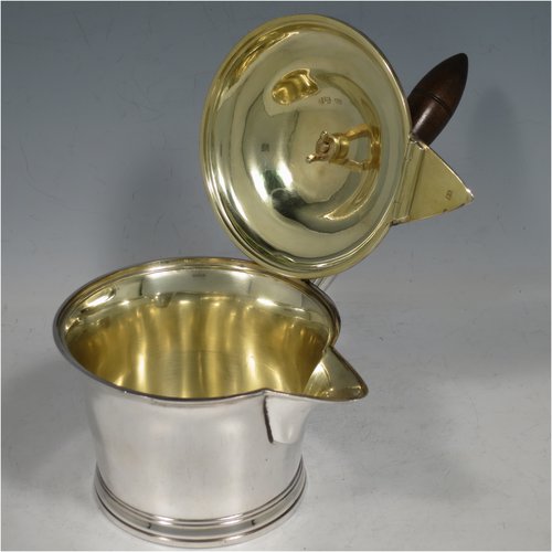 An Antique Georgian Sterling Silver brandy saucepan warmer, having a plain round tapering straight-sided body, a hinged domed lid with a cast goat finial and a hinged sparrow-beak spout, an original wood turned handle, with a gold-gilt interior, and all sitting on a reeded collet foot. Made by Joseph Angell I of London in 1821. The dimensions of this fine hand-made brandy saucepan warmer are height (inc. finial) 13 cms (5 inches), length (inc. handle) 22 cms (8.75 inches), and it weighs approx. 310g (10 troy ounces).   