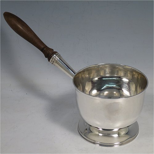 An Antique Georgian Sterling Silver brandy saucepan warmer, having a plain round body with tucked-under belly, an original pinned wood turned handle with heart-shaped cut-card mount, and all sitting on a reeded pedestal foot. Made by John Emes of London in 1805. The dimensions of this fine hand-made brandy saucepan warmer are height of main body 7.5 cms (3 inches), length (inc. handle) 22 cms (8.75 inches), and it weighs approx. 202g (6.5 troy ounces).    