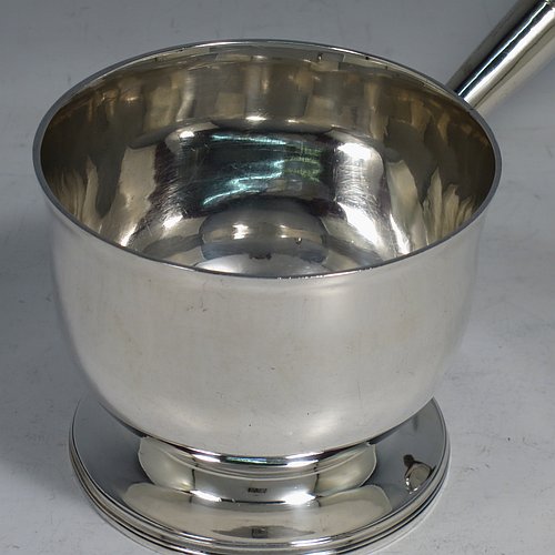 An Antique Georgian Sterling Silver brandy saucepan warmer, having a plain round body with tucked-under belly, an original pinned wood turned handle with heart-shaped cut-card mount, and all sitting on a reeded pedestal foot. Made by John Emes of London in 1805. The dimensions of this fine hand-made brandy saucepan warmer are height of main body 7.5 cms (3 inches), length (inc. handle) 22 cms (8.75 inches), and it weighs approx. 202g (6.5 troy ounces).    