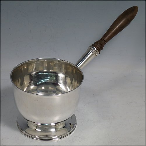 An Antique Georgian Sterling Silver brandy saucepan warmer, having a plain round body with tucked-under belly, an original pinned wood turned handle with heart-shaped cut-card mount, and all sitting on a reeded pedestal foot. Made by John Emes of London in 1805. The dimensions of this fine hand-made brandy saucepan warmer are height of main body 7.5 cms (3 inches), length (inc. handle) 22 cms (8.75 inches), and it weighs approx. 202g (6.5 troy ounces).    