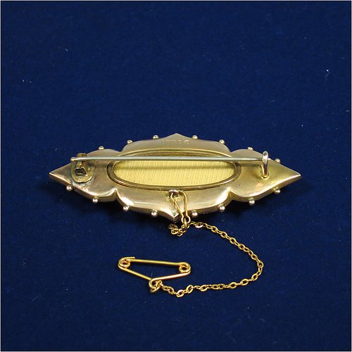 An Antique Victorian Etruscan style 9ct carat gold brooch, having an elongated and shaped oval body, with applied bead decoration, and a stepped oval centre with three old rose-cut diamonds, and the back having a pin with oval locket and glass cover, and an attached security chain. Made in ca. 1880. The dimensions of this fine antique gold brooch are length 5 cms (2 inches), width 2.5 cms (1 inch), and it weighs approx. 7g.