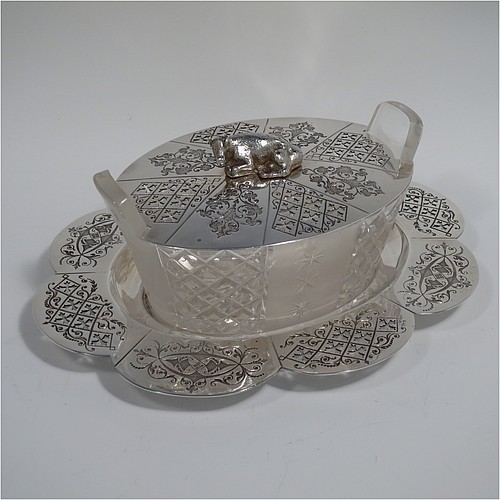 An Antique Victorian Silver Plated butter dish and cover, having an oval crystal body with panels of hand-cut and frosted decoration, a lift-off hand-engraved lid with a cast cow finial, and all sitting on a hand-engraved and pierced lobed oval dish. Made in ca. 1880. The dimensions of this fine hand-made antique silver plated butter dish are height 8 cms (3 inches), length 23 cms (9 inches), and width 19 cms (7.5 inches).    