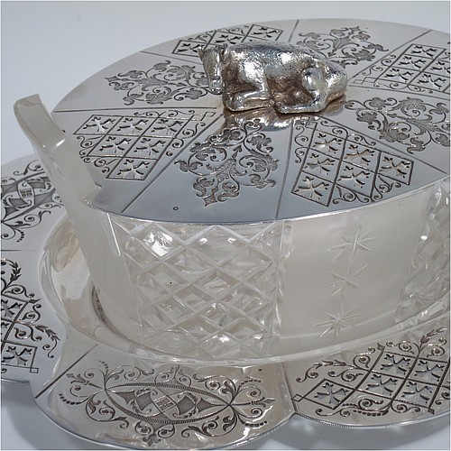 An Antique Victorian Silver Plated butter dish and cover, having an oval crystal body with panels of hand-cut and frosted decoration, a lift-off hand-engraved lid with a cast cow finial, and all sitting on a hand-engraved and pierced lobed oval dish. Made in ca. 1880. The dimensions of this fine hand-made antique silver plated butter dish are height 8 cms (3 inches), length 23 cms (9 inches), and width 19 cms (7.5 inches).    