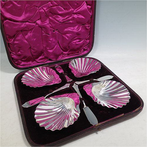 An Antique Victorian Sterling Silver set of four butter shells, having traditional scallop shapes, and sitting on three cast shell feet, together with four original butter knives in the Albany pattern, and all sitting in an original purple satin and velvet-lined presentation box. All made by Frances Higgins of London in 1884. The dimensions of this fine hand-made set of antique silver butter shells are length 12 cms (4.75 inches), width 10 cms (4 inches), with a total weight of approx. 385g (12.4 troy ounces).   